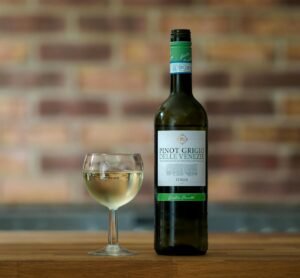 A bottle of Pinot Grigio and a filled glass on a wooden surface indoors.