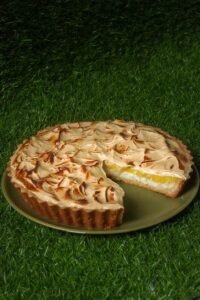 Sliced lemon meringue pie on green grass, showcasing creamy filling and toasted peaks.