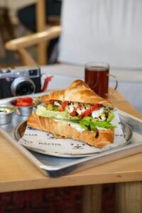 Appetizing croissant sandwich with vegetables on a tray in a cozy café setting.