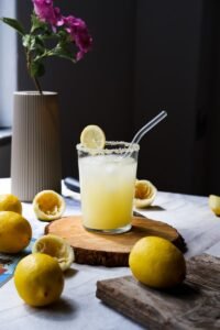 a glass of orange juice with lemons and a spoon on a cutting board