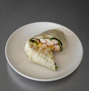 Close-up of a tasty grilled chicken wrap with fresh ingredients on a plate.