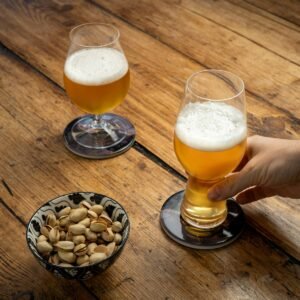 A person holding a glass of beer next to a bowl of nuts